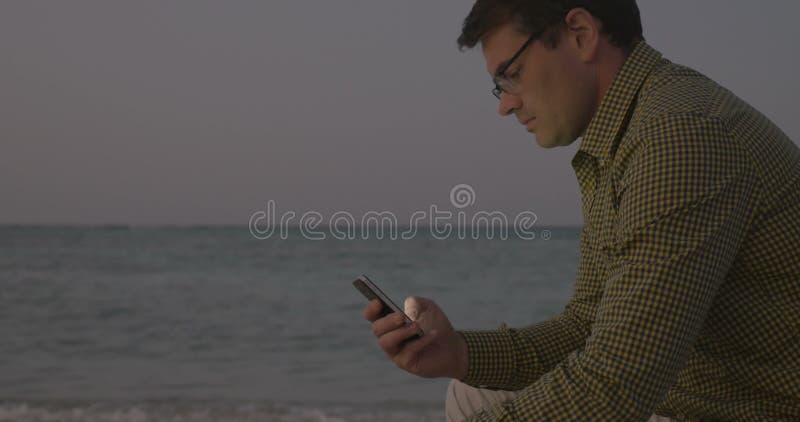 Giovane che utilizza Smart Phone dal mare nella sera