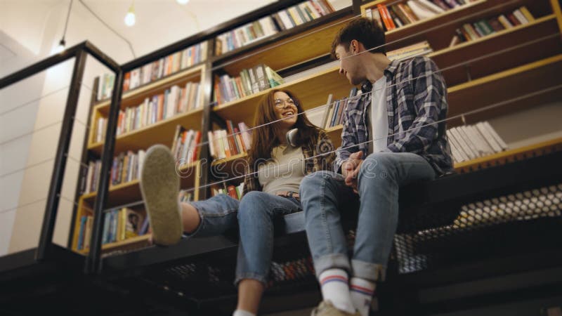 Giovane coppia che si gode un momento tranquillo insieme in una comoda biblioteca piena di libri nel pomeriggio archivi video