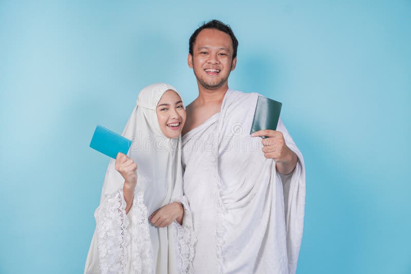Giovane coppia musulmana asiatica sorridente indossa ihram e un abito di preghiera con il passaporto isolato da sfondo blu. concet fotografia stock libera da diritti
