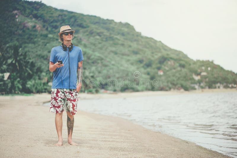 Giovane in cuffie ed occhiali da sole alla spiaggia che ascolta la musica fotografia stock Giovane in cuffie ed occhiali da sole alla spiaggia che ascolta la musica fotografia stock