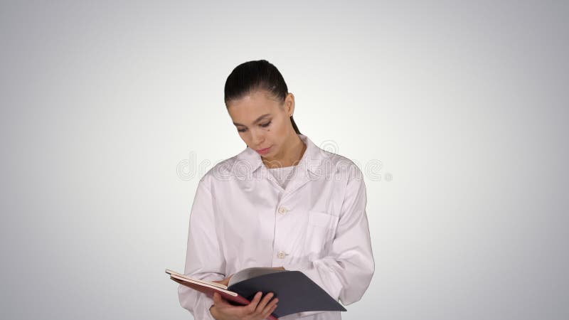 Giovane documentazione della lettura della donna di medico mentre camminando sul fondo di pendenza immagine stock Giovane documentazione della lettura della donna di medico mentre camminando sul fondo di pendenza immagine stock
