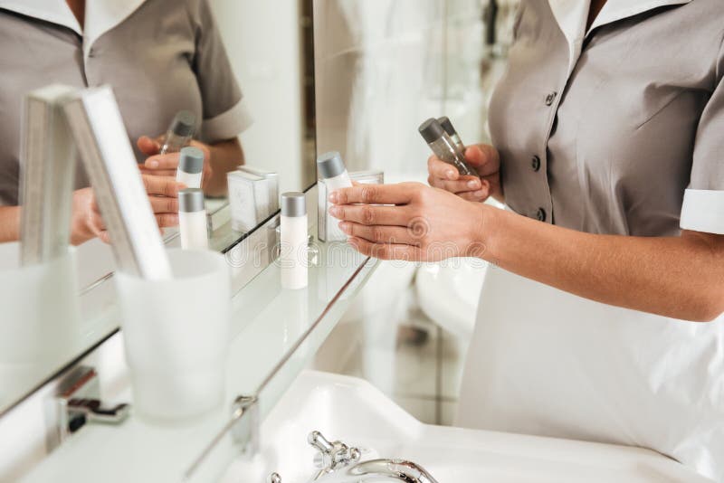 Giovane domestica dell'hotel che mette gli accessori del bagno in un bagno immagine stock Giovane domestica dell'hotel che mette gli accessori del bagno in un bagno immagine stock