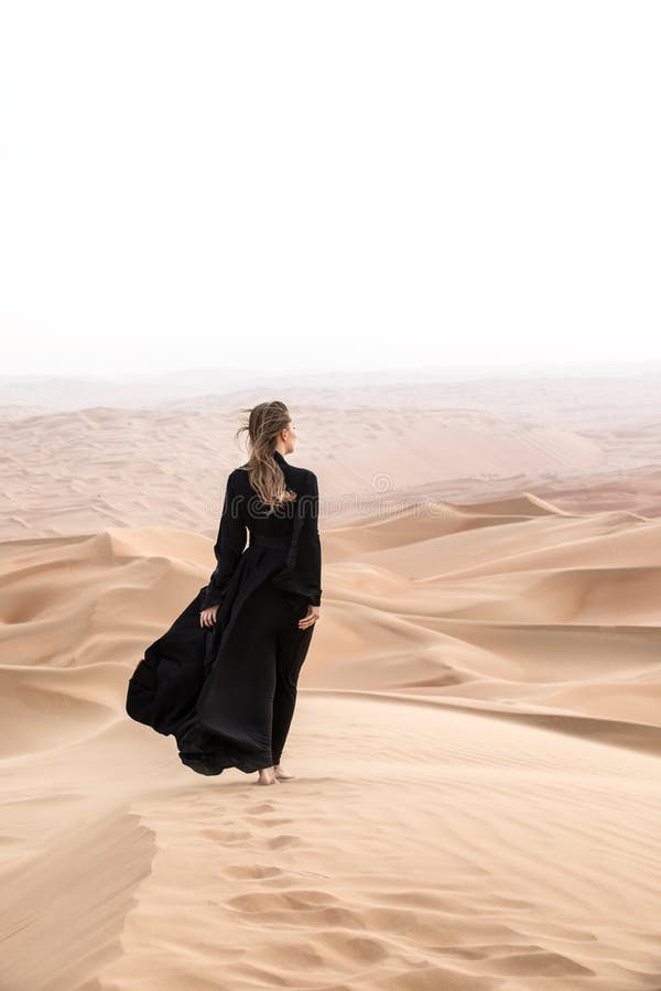 Giovane donna in Abaya che posa nel paesaggio del deserto fotografia stock libera da diritti Giovane donna in Abaya che posa nel paesaggio del deserto fotografia stock libera da diritti