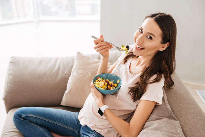 Giovane donna abbastanza incinta che mangia prima colazione sana immagini stock libere da diritti Giovane donna abbastanza incinta che mangia prima colazione sana immagini stock libere da diritti
