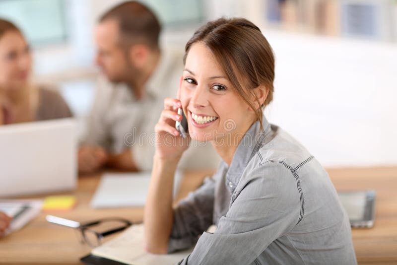 Giovane donna all'ufficio che negozia sul telefono immagini stock libere da diritti Giovane donna all'ufficio che negozia sul telefono immagini stock libere da diritti