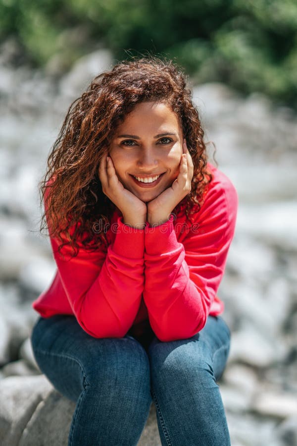 Giovane donna allegra con capelli ricci che posano mentre sedendosi fuori immagini stock libere da diritti Giovane donna allegra con capelli ricci che posano mentre sedendosi fuori immagini stock libere da diritti