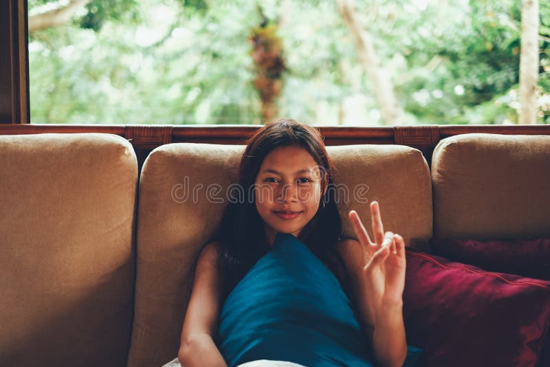 Giovane donna asiatica durante la vacanza che si rilassa sul sofà con la grande finestra dietro lei donna sulle vacanze estive in fotografia stock Giovane donna asiatica durante la vacanza che si rilassa sul sofà con la grande finestra dietro lei donna sulle vacanze estive in fotografia stock