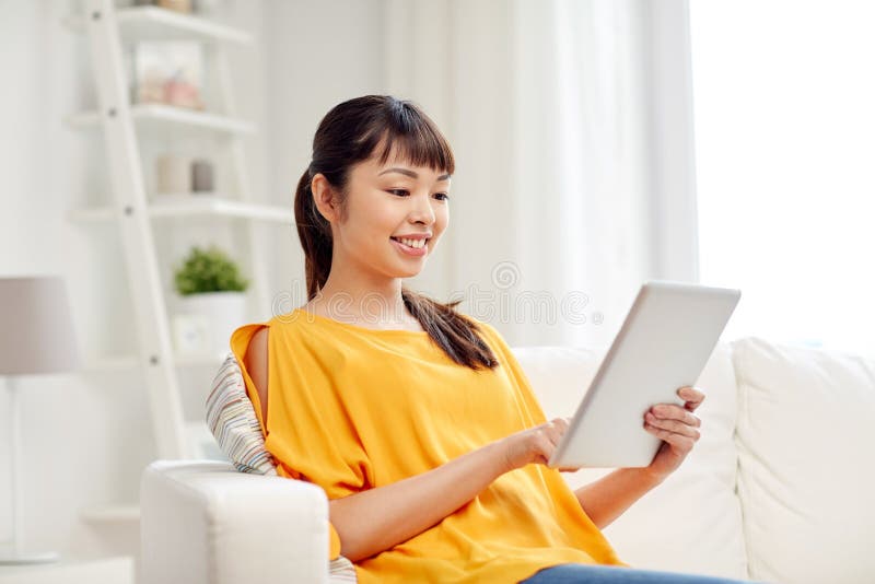 Giovane donna asiatica felice con il pc della compressa a casa fotografia stock Giovane donna asiatica felice con il pc della compressa a casa fotografia stock