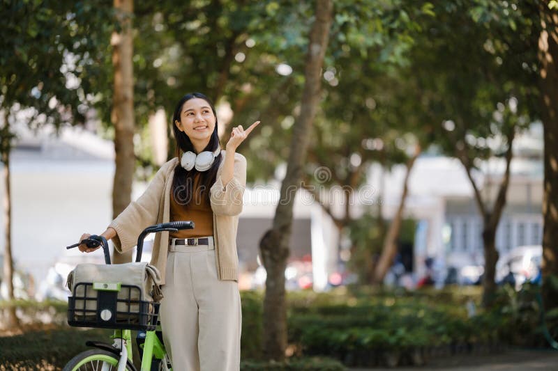 Giovane donna asiatica usa cuffie mentre va in bicicletta nel parco cittadino fotografie stock