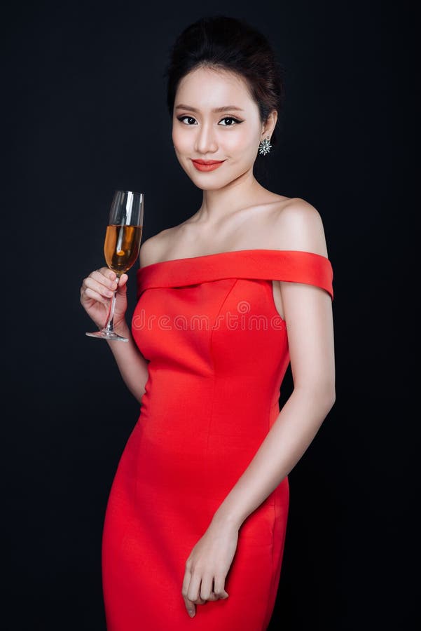 Giovane donna asiatica in vestito rosso di lusso con vetro dei wi scintillanti fotografia stock libera da diritti Giovane donna asiatica in vestito rosso di lusso con vetro dei wi scintillanti fotografia stock libera da diritti