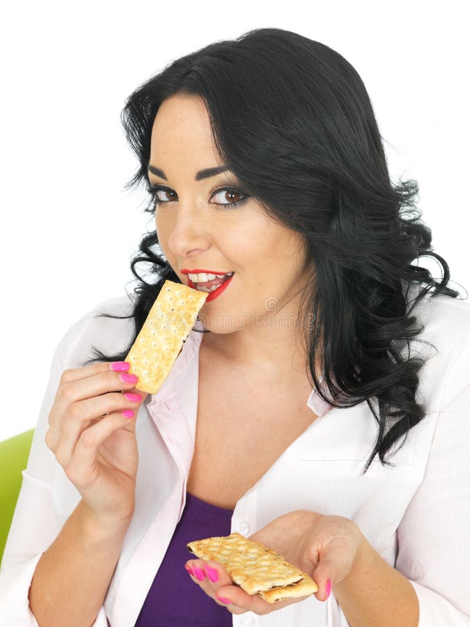 Young Healthy Attractive Woman with long black curly hair and hispanic or european features, looking at camera, Eating Thin mixed dried fruit bars, healthy snacking or dieting, low calorie intake, wearing a white shirt with purple top, shot against a white background. Young Healthy Attractive Woman with long black curly hair and hispanic or european features, looking at camera, Eating Thin mixed dried fruit bars, healthy snacking or dieting, low calorie intake, wearing a white shirt with purple top, shot against a white background.