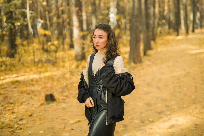 Giovane donna attraente che cammina nel parco autunnale felice umore e moda stile moda e capelli castani ricci. stagione di caduta immagini stock