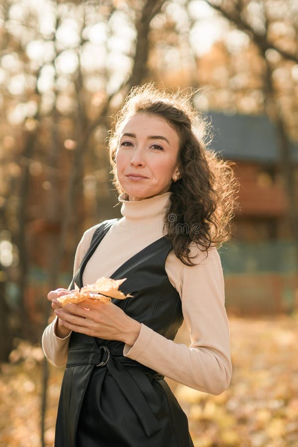 Giovane donna attraente che cammina nel parco autunnale felice umore e moda stile moda e capelli castani ricci. stagione di caduta fotografie stock