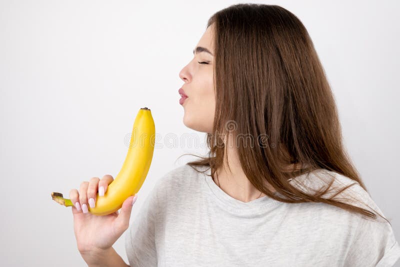 Young attractive woman holding banana like a gun in her hand looking decisive standing on isolated white background dietology and nutrition. Young attractive woman holding banana like a gun in her hand looking decisive standing on isolated white background dietology and nutrition.