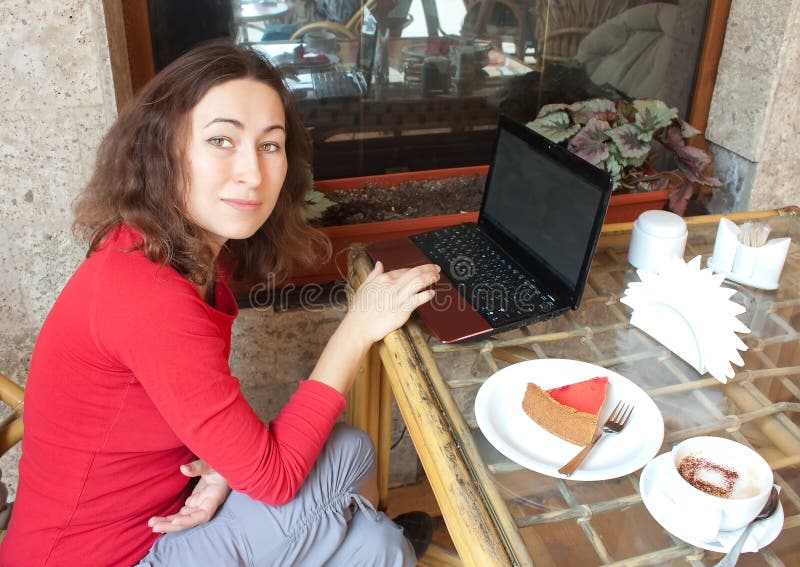 Giovane donna attraente in un caffè con un computer portatile immagine stock Giovane donna attraente in un caffè con un computer portatile immagine stock