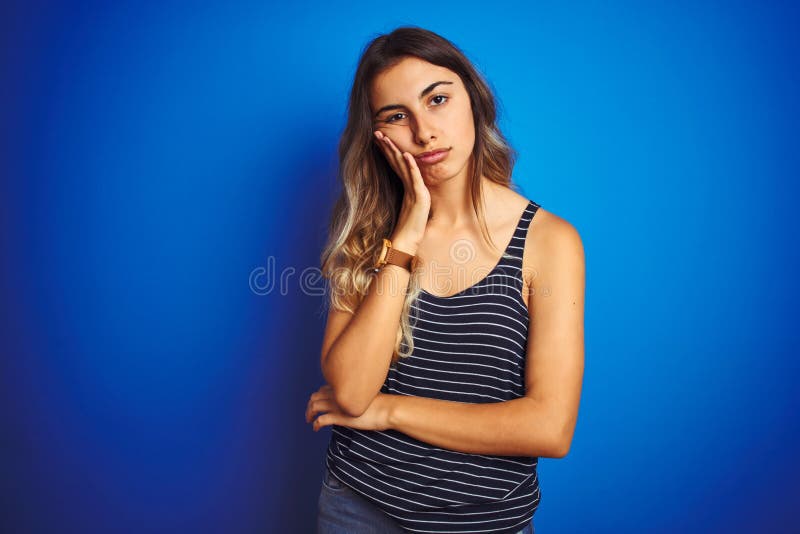 Giovane donna bella con una camicia a strisce su uno sfondo azzurro isolato pensando di essere stanca e annoiata dalla depressione immagine stock