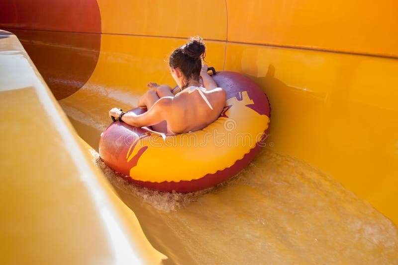 Giovane donna in bikini su un galleggiante gonfiabile di gomma indietro su un acquascivolo, giocando e divertendosi allo stagno d