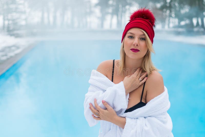 Giovane donna bionda in accappatoio e capanna rossa vicino alla piscina all'aperto all'inverno immagine stock Giovane donna bionda in accappatoio e capanna rossa vicino alla piscina all'aperto all'inverno immagine stock