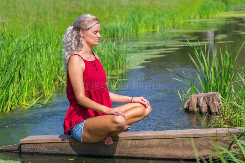 Giovane donna bionda che medita all'acqua in natura fotografia stock libera da diritti Giovane donna bionda che medita all'acqua in natura fotografia stock libera da diritti