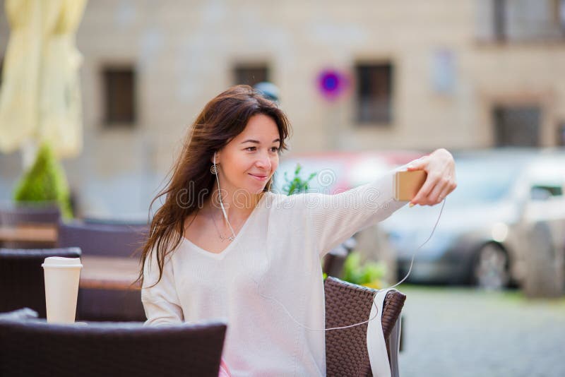 Giovane donna caucasica che invia messaggio e che prende autoritratto in caffè all'aperto La ragazza felice gode dell'ora legale fotografia stock libera da diritti Giovane donna caucasica che invia messaggio e che prende autoritratto in caffè all'aperto La ragazza felice gode dell'ora legale fotografia stock libera da diritti