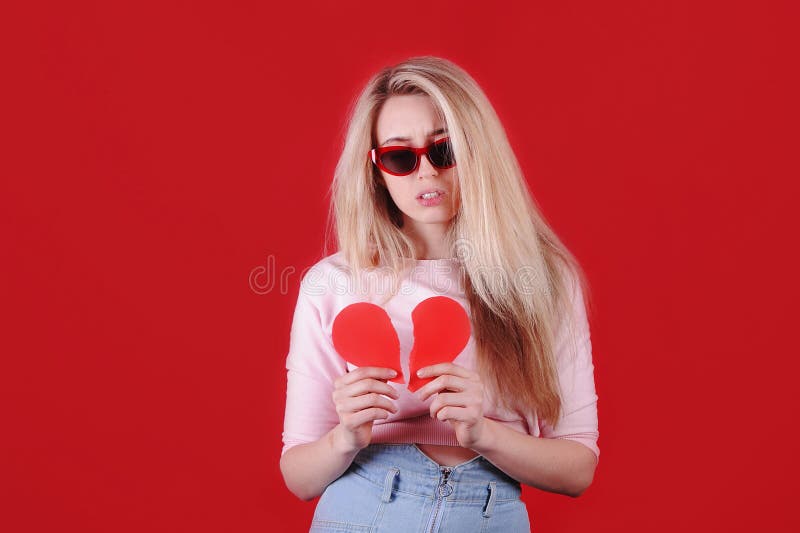 Giovane donna caucasica con occhiali da sole con cuore rosso rotto in mano fotografia stock Giovane donna caucasica con occhiali da sole con cuore rosso rotto in mano fotografia stock