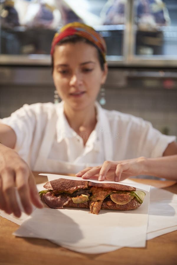 Giovane donna che avvolge un panino all'ghiottoneria contro, verticale immagine stock libera da diritti Giovane donna che avvolge un panino all'ghiottoneria contro, verticale immagine stock libera da diritti