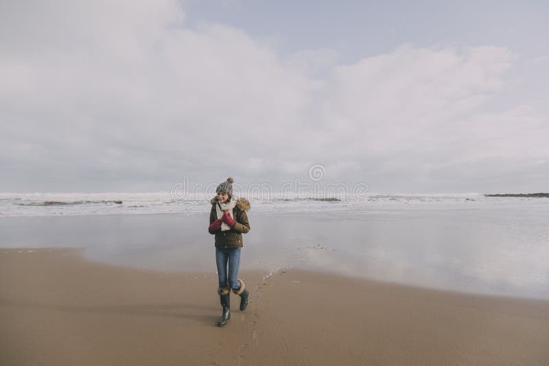 Giovane donna che cammina lungo la spiaggia di inverno fotografie stock Giovane donna che cammina lungo la spiaggia di inverno fotografie stock