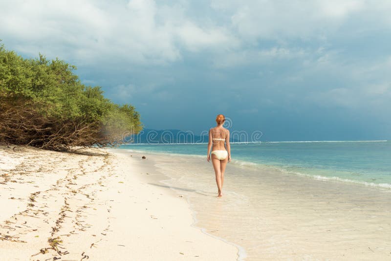 Giovane donna che cammina lungo la spiaggia tropicale