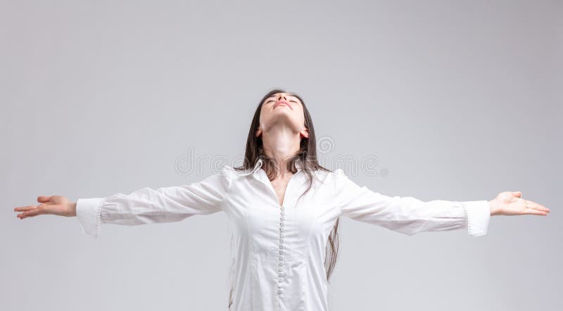 Young woman enjoying a moment of peace standing with outstretched arms and closed eyes with a serene expression and head tilted back over grey. Young woman enjoying a moment of peace standing with outstretched arms and closed eyes with a serene expression and head tilted back over grey