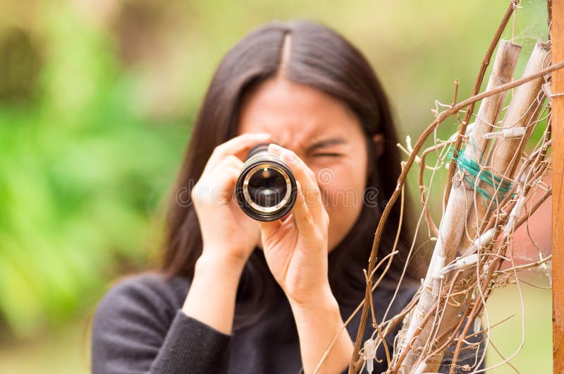 Giovane donna che guarda tramite il cannocchiale nero nella foresta in un fondo vago fotografia stock libera da diritti Giovane donna che guarda tramite il cannocchiale nero nella foresta in un fondo vago fotografia stock libera da diritti