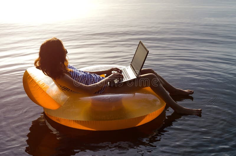 Giovane donna che lavora ad un computer portatile nell'acqua su un ri gonfiabile fotografia stock libera da diritti Giovane donna che lavora ad un computer portatile nell'acqua su un ri gonfiabile fotografia stock libera da diritti