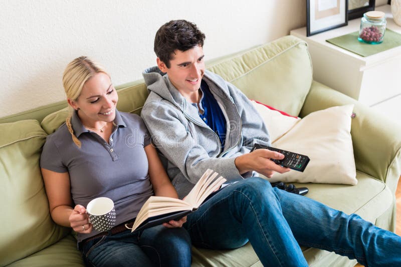 Giovane donna che legge un libro accanto al suo ragazzo che guarda TV immagini stock Giovane donna che legge un libro accanto al suo ragazzo che guarda TV immagini stock