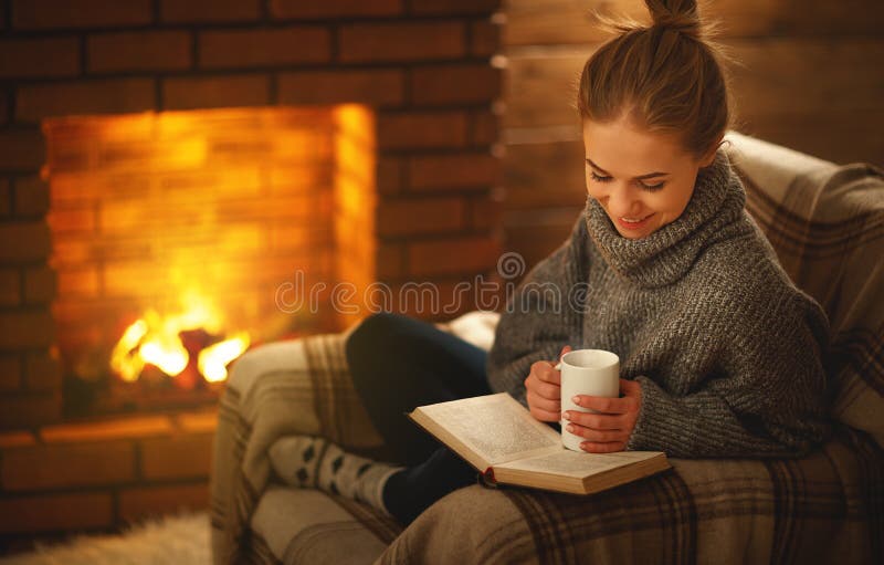 Giovane donna che legge un libro dal camino su un evenin di inverno