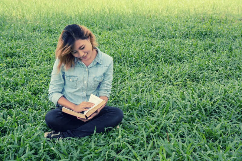 Giovane donna che legge un libro nel parco sull'erba immagine stock Giovane donna che legge un libro nel parco sull'erba immagine stock