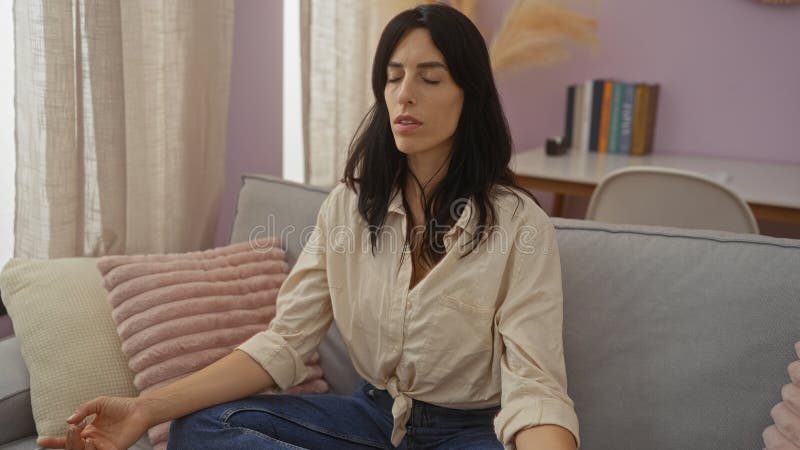 Giovane donna che medita al chiuso in un soggiorno sereno circondata da un comodo arredamento e cuscini morbidi che suggeriscono r fotografia stock libera da diritti