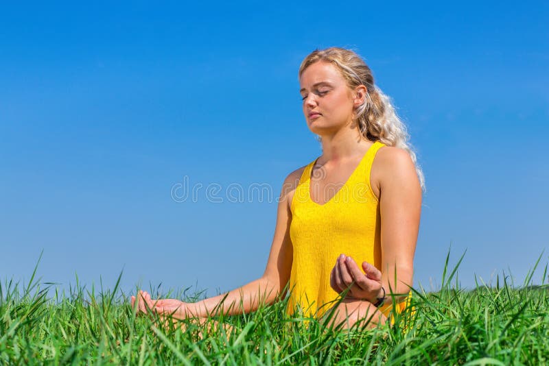 Giovane donna che medita nell'erba con cielo blu fotografia stock libera da diritti Giovane donna che medita nell'erba con cielo blu fotografia stock libera da diritti