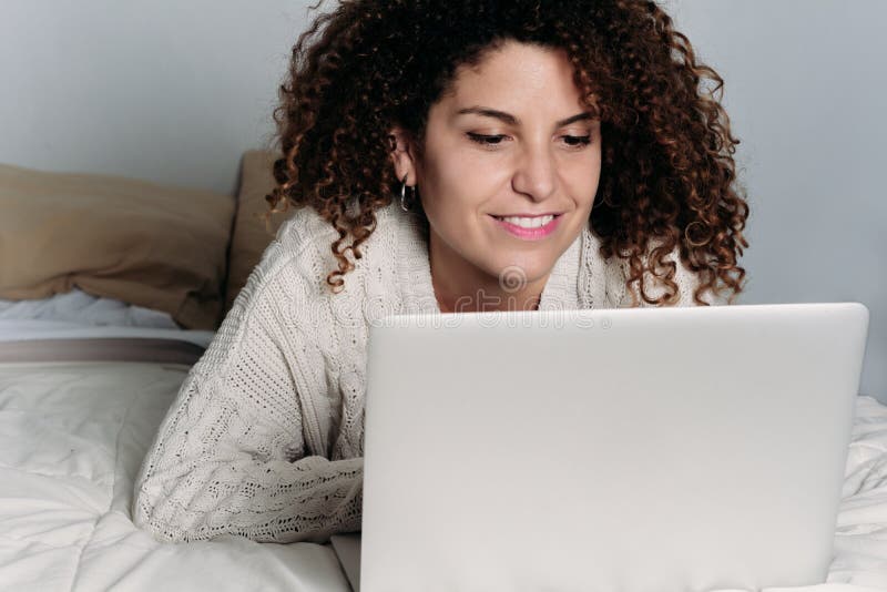 Giovane donna che per mezzo del suo computer portatile sul letto fotografia stock Giovane donna che per mezzo del suo computer portatile sul letto fotografia stock