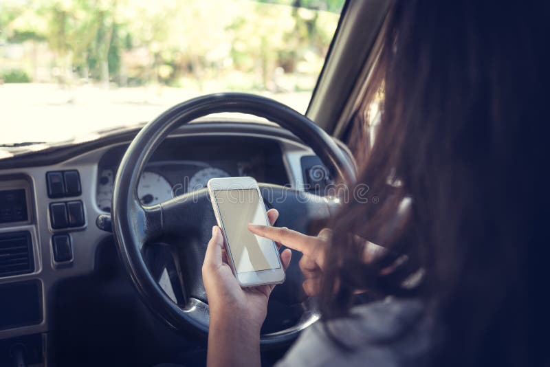 Giovane donna che per mezzo dello Smart Phone mentre conducendo un'automobile fotografia stock Giovane donna che per mezzo dello Smart Phone mentre conducendo un'automobile fotografia stock