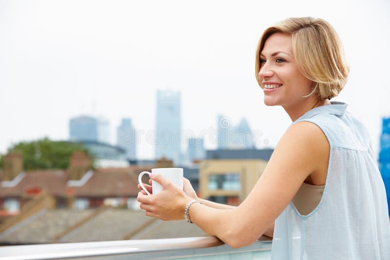 Giovane donna che si rilassa sul terrazzo del tetto con la tazza di caffè fotografia stock Giovane donna che si rilassa sul terrazzo del tetto con la tazza di caffè fotografia stock
