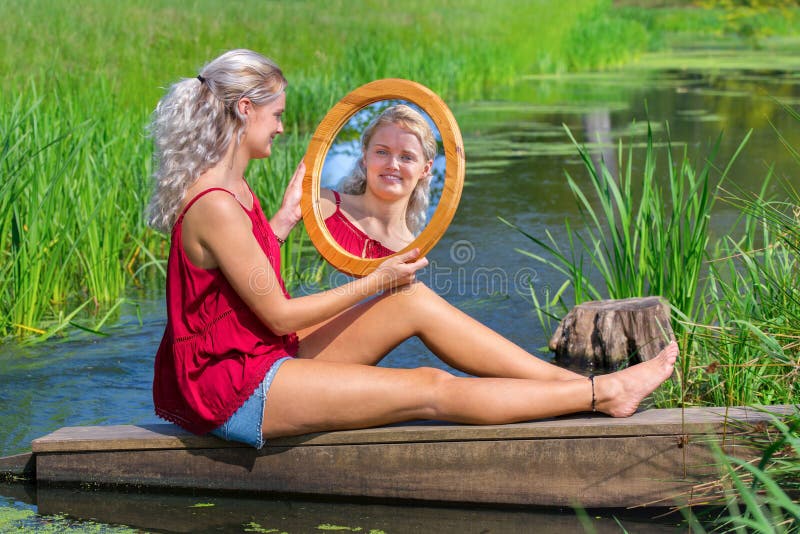 Giovane donna che si siede con lo specchio all'acqua naturale immagine stock Giovane donna che si siede con lo specchio all'acqua naturale immagine stock