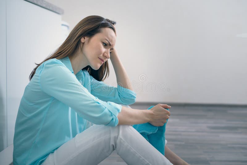 Giovane donna che si siede sul pavimento della cucina che tiene la sua testa e che grida, ribaltamento, triste, depresso fotografia stock Giovane donna che si siede sul pavimento della cucina che tiene la sua testa e che grida, ribaltamento, triste, depresso fotografia stock