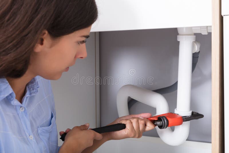 Giovane donna che stringe il tubo del lavandino con la chiave inglese fotografia stock libera da diritti Giovane donna che stringe il tubo del lavandino con la chiave inglese fotografia stock libera da diritti