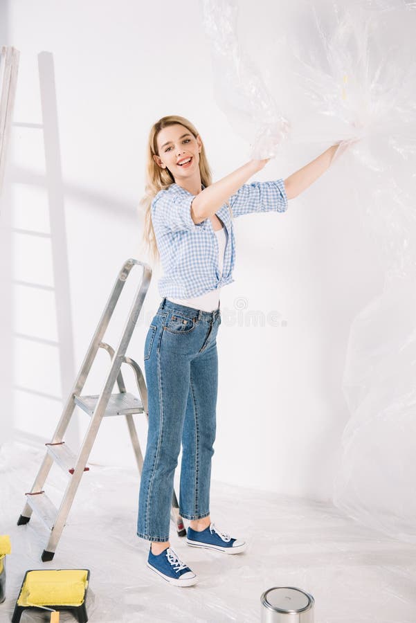 Giovane donna che tiene in mano il cellophane mentre si prepara a dipingere il muro immagine stock