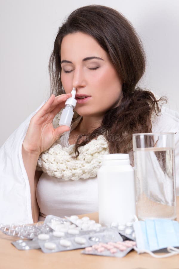 Young attractive woman using nasal spray in her living room. Young attractive woman using nasal spray in her living room