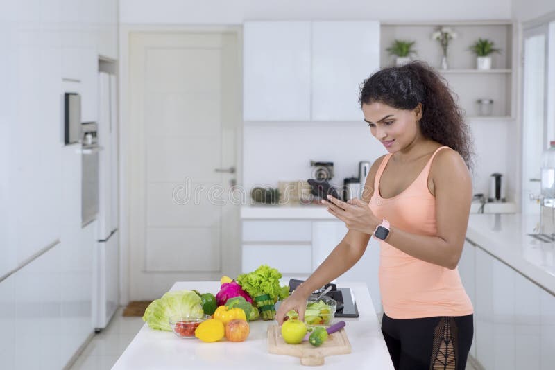 Giovane donna che usa uno smartphone in cucina immagini stock libere da diritti