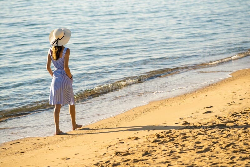 Giovane donna con cappello di paglia e vestito che cammina da sola su una spiaggia deserta di sabbia sulla riva del mare. una turi
