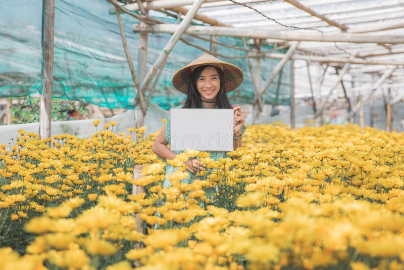 Giovane donna con il bordo bianco in bianco nell'azienda agricola del fiore fotografia stock libera da diritti Giovane donna con il bordo bianco in bianco nell'azienda agricola del fiore fotografia stock libera da diritti