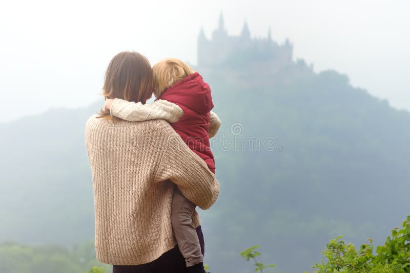 Giovane donna con il piccolo bambino che ammira vista del castello famoso di Hohenzollern al giorno nebbioso Viaggio della famigl immagini stock Giovane donna con il piccolo bambino che ammira vista del castello famoso di Hohenzollern al giorno nebbioso Viaggio della famigl immagini stock
