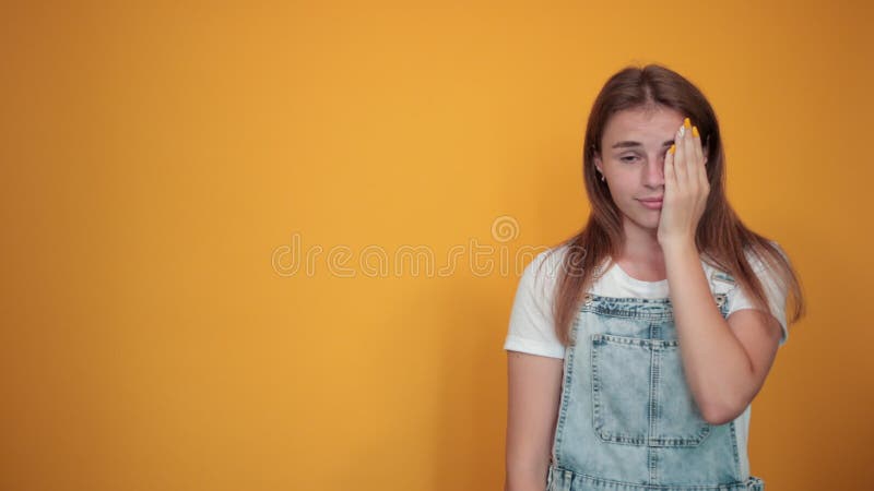 Giovane donna con una maglietta bianca sullo sfondo arancione mostra emozioni