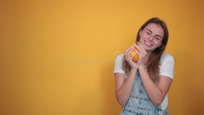 Giovane donna con una maglietta bianca sullo sfondo arancione mostra emozioni